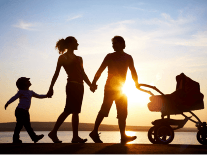 Father pushing a stroller while holding his wife's hand as she holds their young child's hand